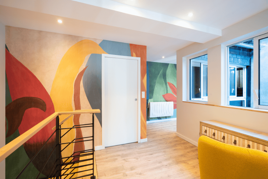Peinture décorative intérieure avec fresques murales colorées et parquet dans un couloir à Montardon – Tuheil Établissement