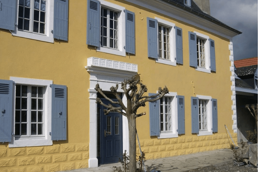 Ravalement de façade maison ancienne avec enduit jaune ocre et volets bleus peints à Monein – Tuheil Établissement