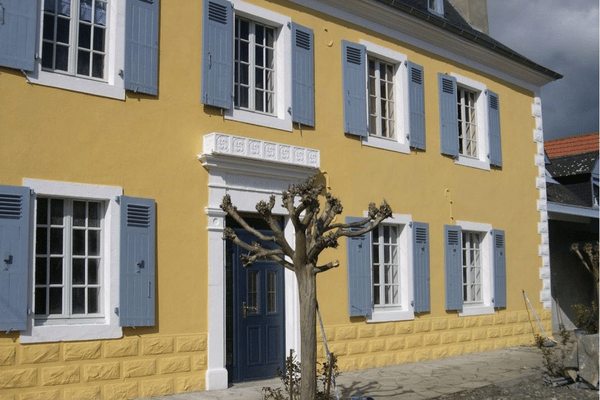 Ravalement de façade avec enduit teinté jaune et encadrements blancs sur maison ancienne à Orthez – Tuheil Établissement